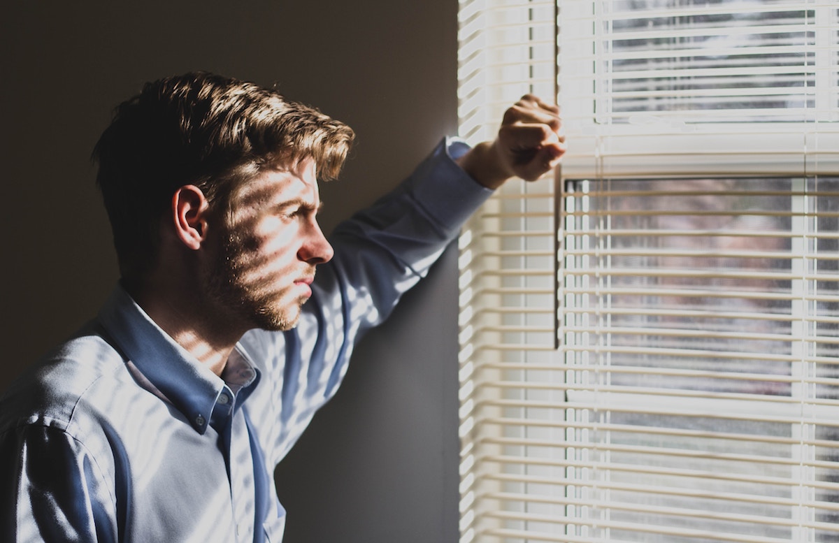 Man looking out window sadly.