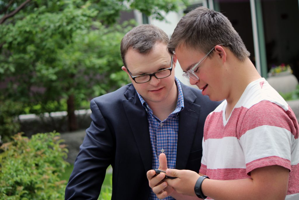 Two men with Down syndrome working on their phones.