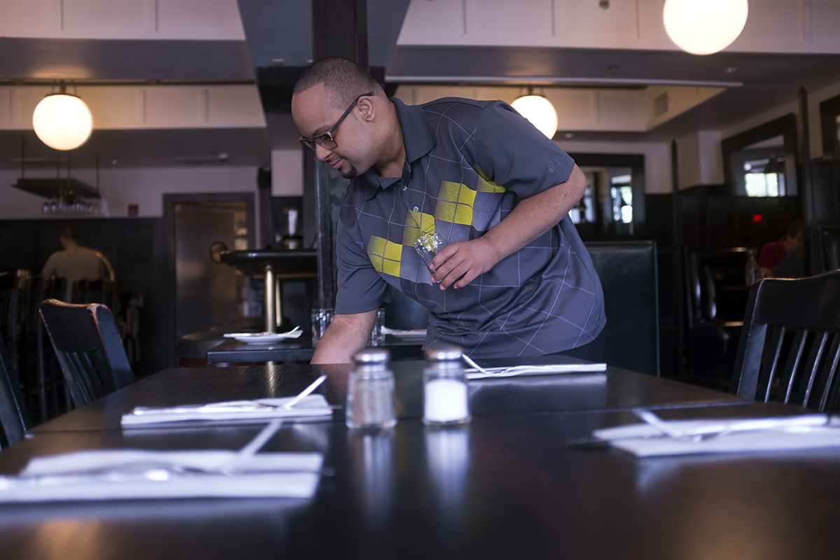 Young black man with Down syndrome clearing dishes at a restaurant.