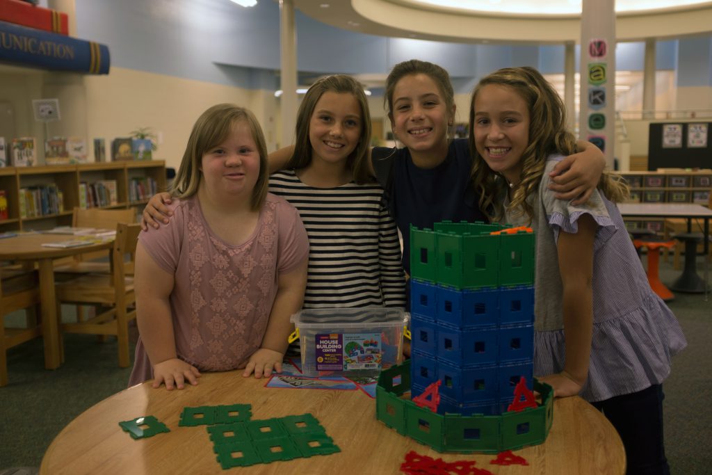 Photo of 4 girls with their arms each other at school, including one girl with Down syndrome.