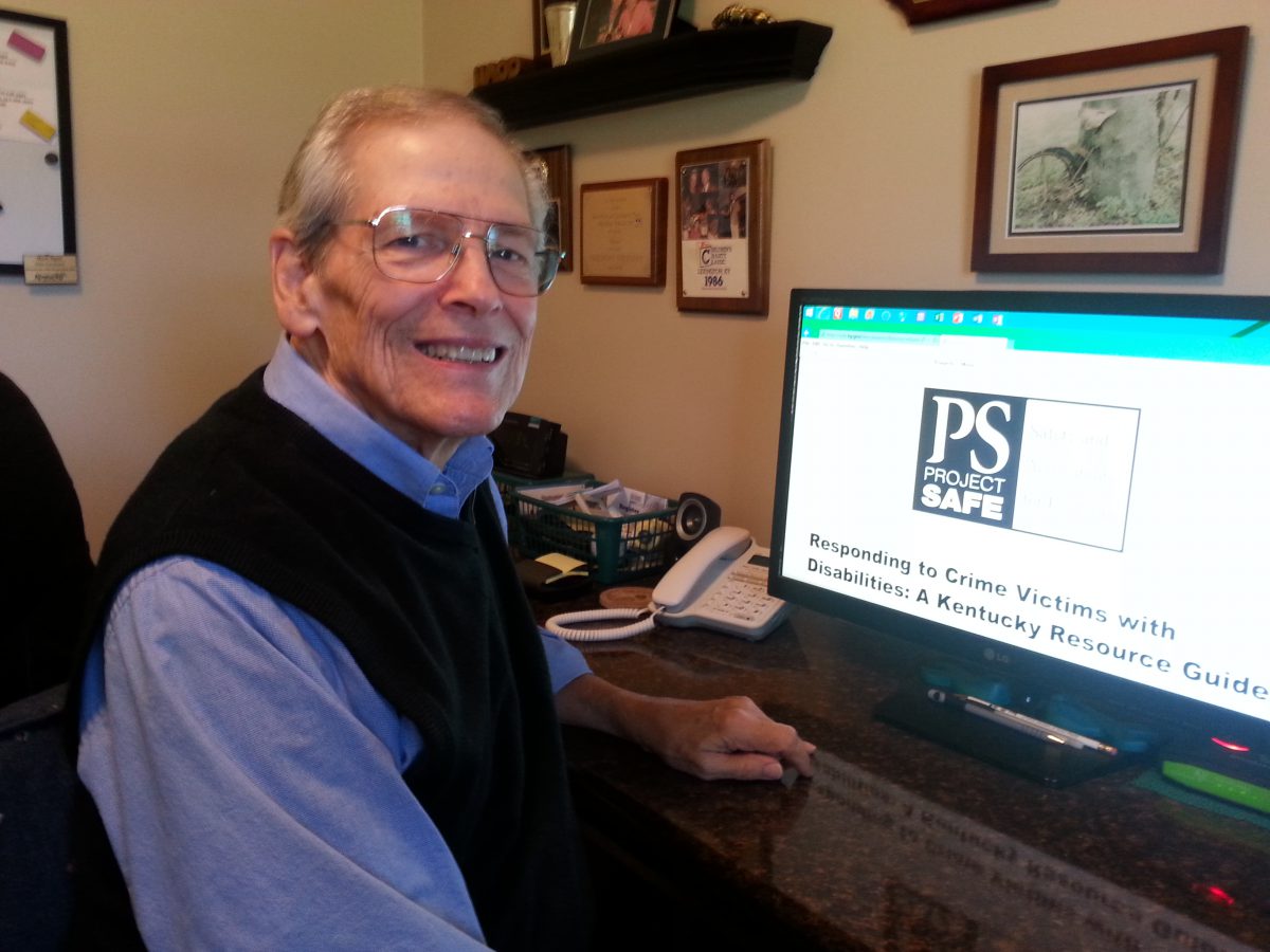 Norb Ryan, white older man wearing a knit vest, at a computer smiling at the camera