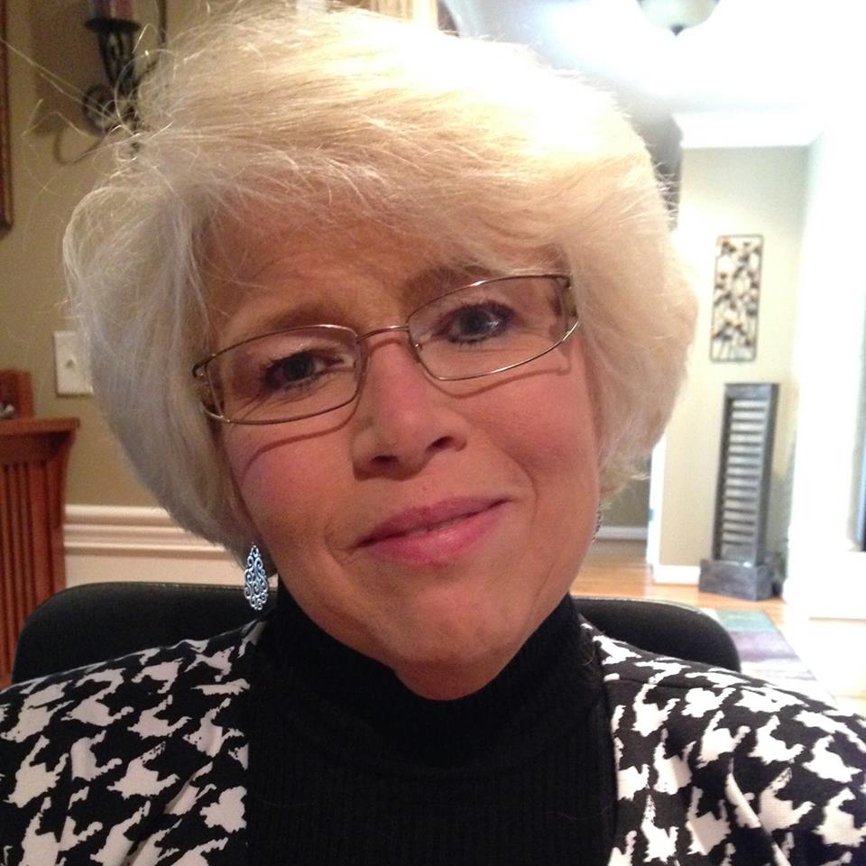 Photo of Marlene Huff, a white woman with white hair and glasses smiling and wearing black and white