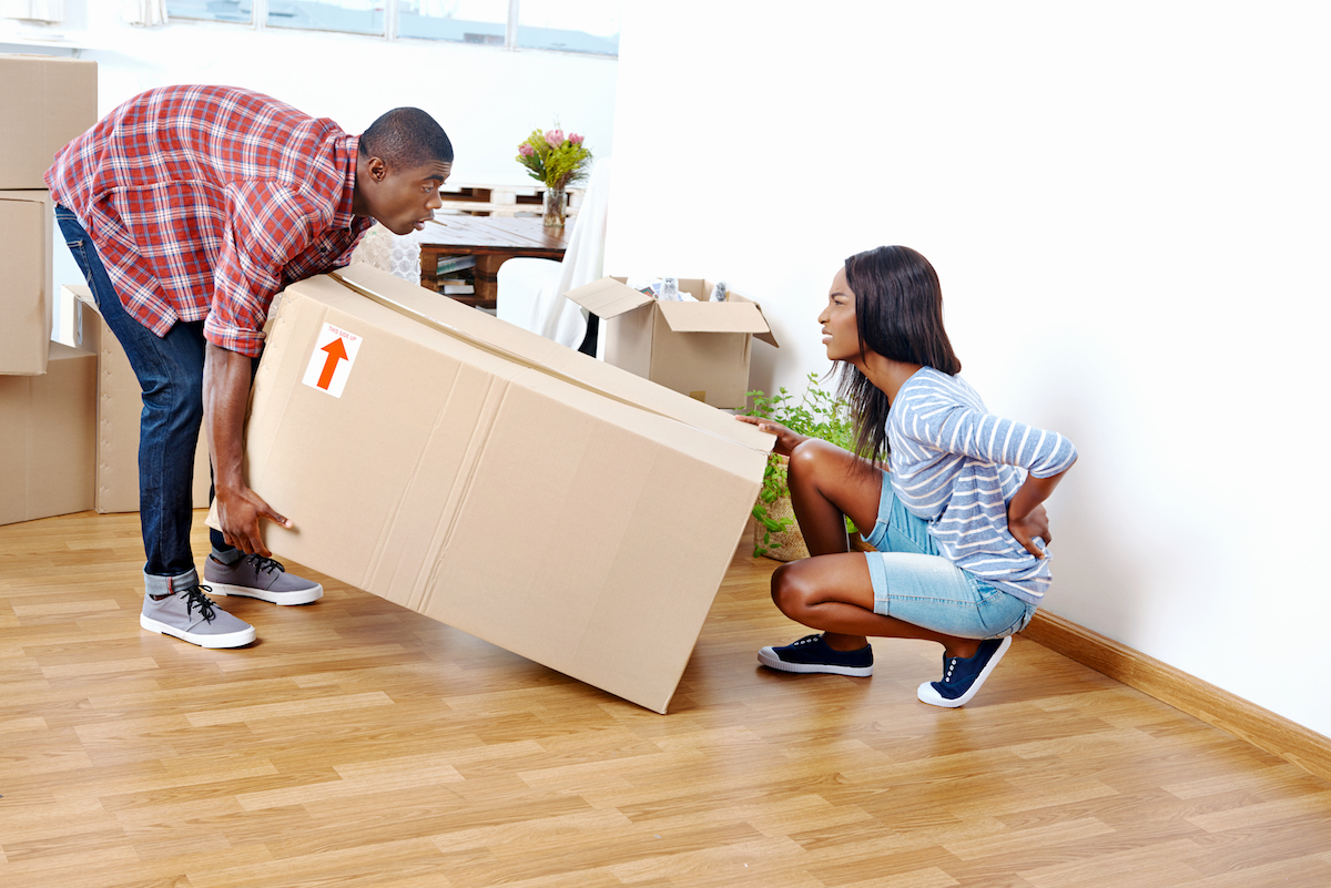 Man and woman lifting a box and woman grabbing back in pain.