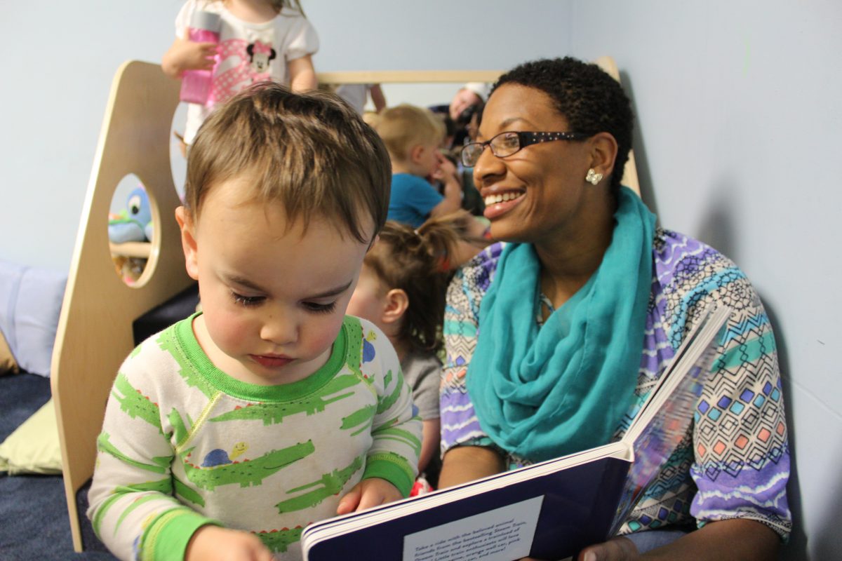 Child reading a book with teacher.