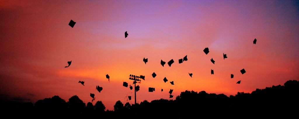 black graduation caps being thrown in the sunset sky