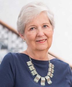 Allison Carll White's headshot. She is wearing a navy shirt and silver necklace. She has short, silver hair.