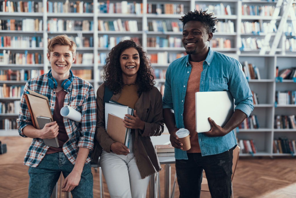 3 people standing in front of book stacks holding books