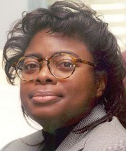 Debra Harley headshot. She is wearing a grey blazer. She has long, curly black hair and is wearing glasses.