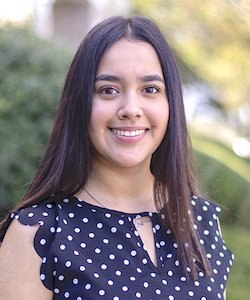 Adareli Ojeda staff photo. She is wearing a black and white polka dot blouse and has long, dark hair. She is standing in front of trees and smiling at the camera.