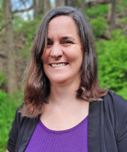 Julie Halitzka staf photo. She has shoulder-length brown hair and is wearing a purple blouse with a black sweater. She is smiling at the camera.