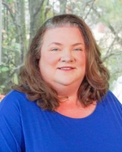 Michele Laur staff photo. She is wearing a UK blue blouse and has shoulder-length curly, brown hair and is smiling at the camera