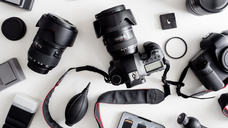 table covered in photography supplies, like cameras, lenses, neck straps, and more