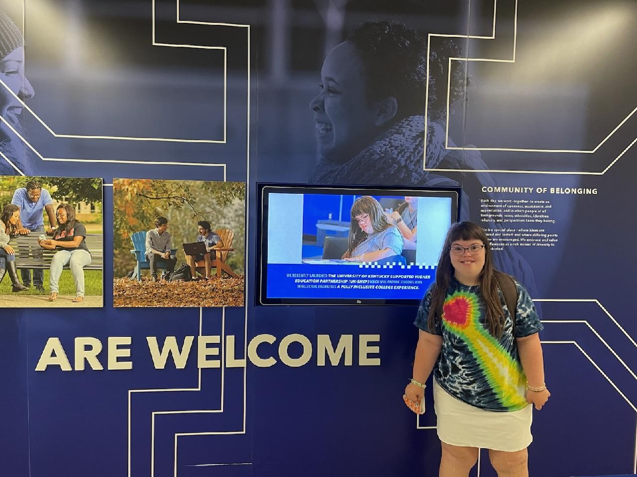 A smiling female student standing next to a screen displaying information about the UK-SHEP project