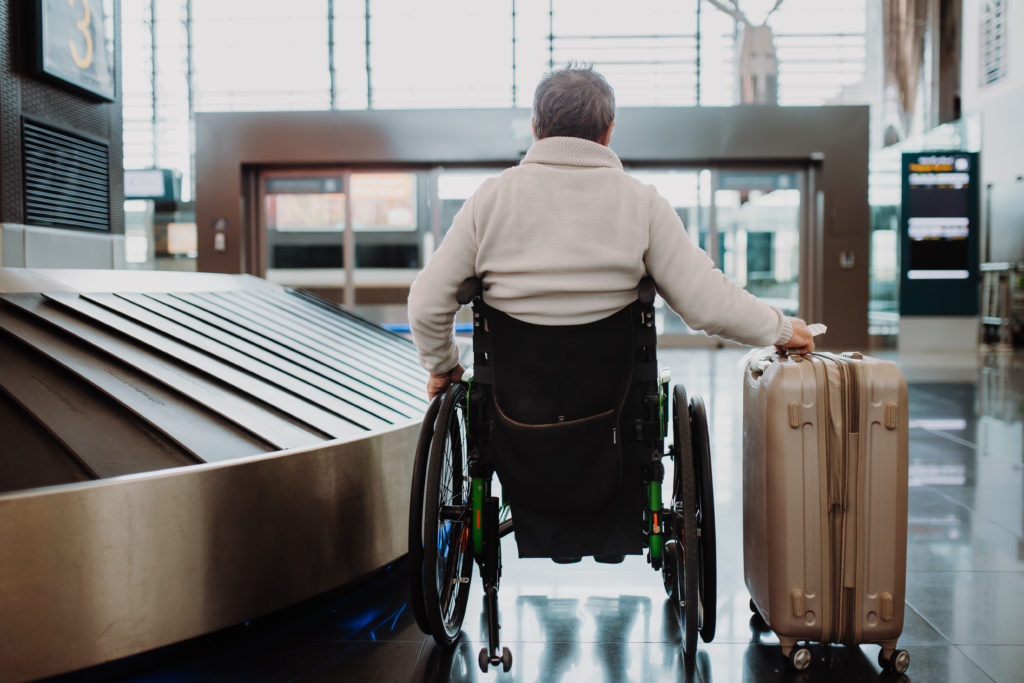 Rear view of a man on wheelchair at airport with his luggage.