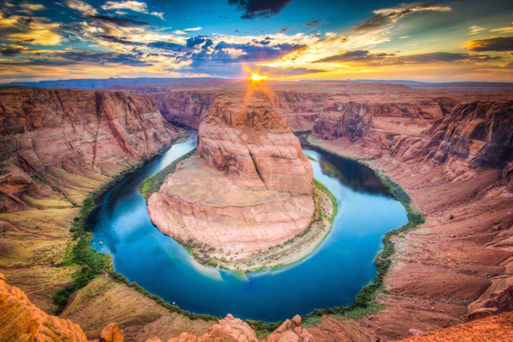 rock formations with bright horizon, with a circular body of bright blue water in the middle, and a tall rock formation in the center or the water