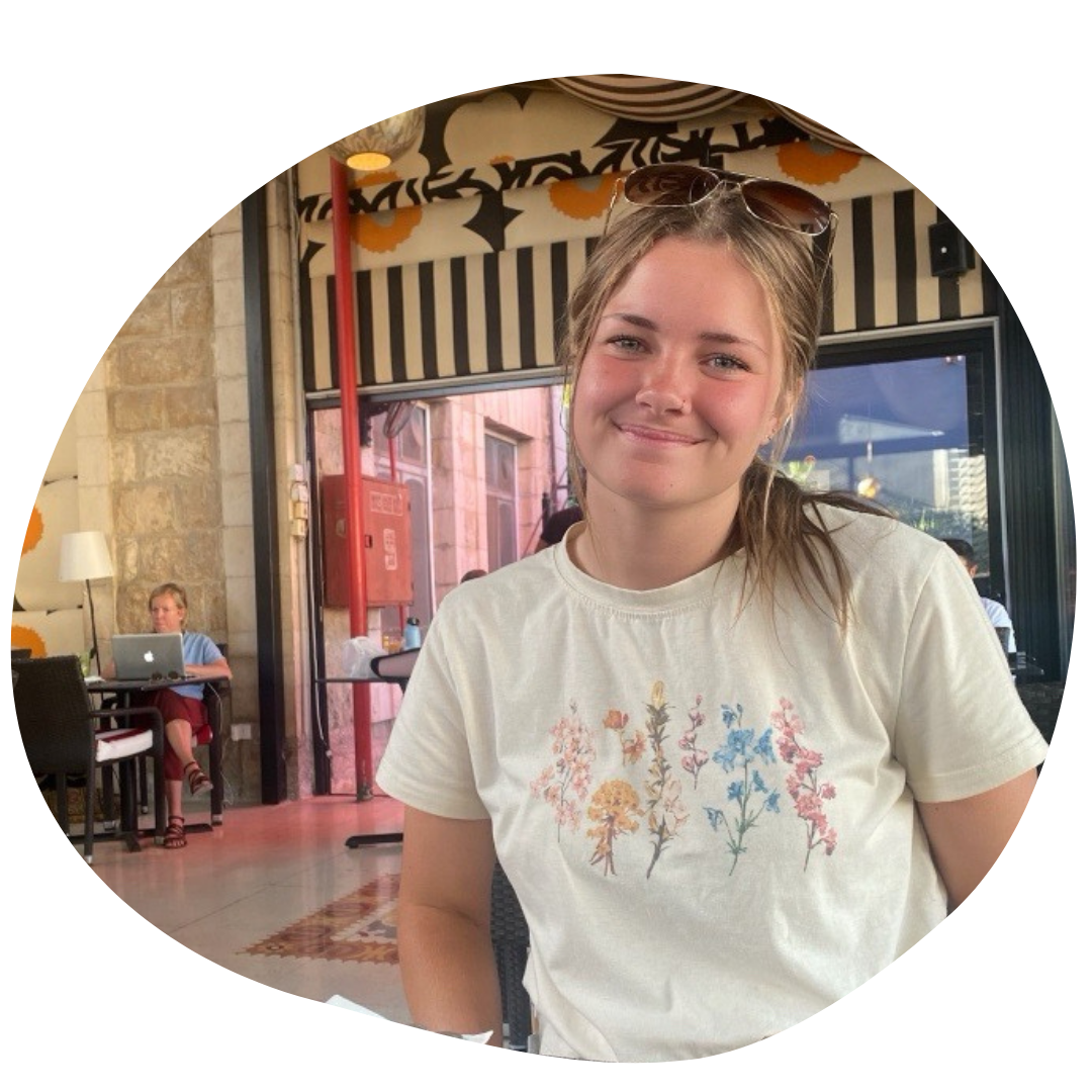 haliegh bokros staff photo. she is smiling at the camera at a restaurant, wearing a white t-shirt with flowers